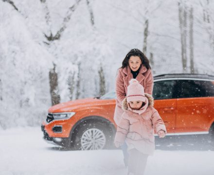 Mother with little daughter in a winter park by car